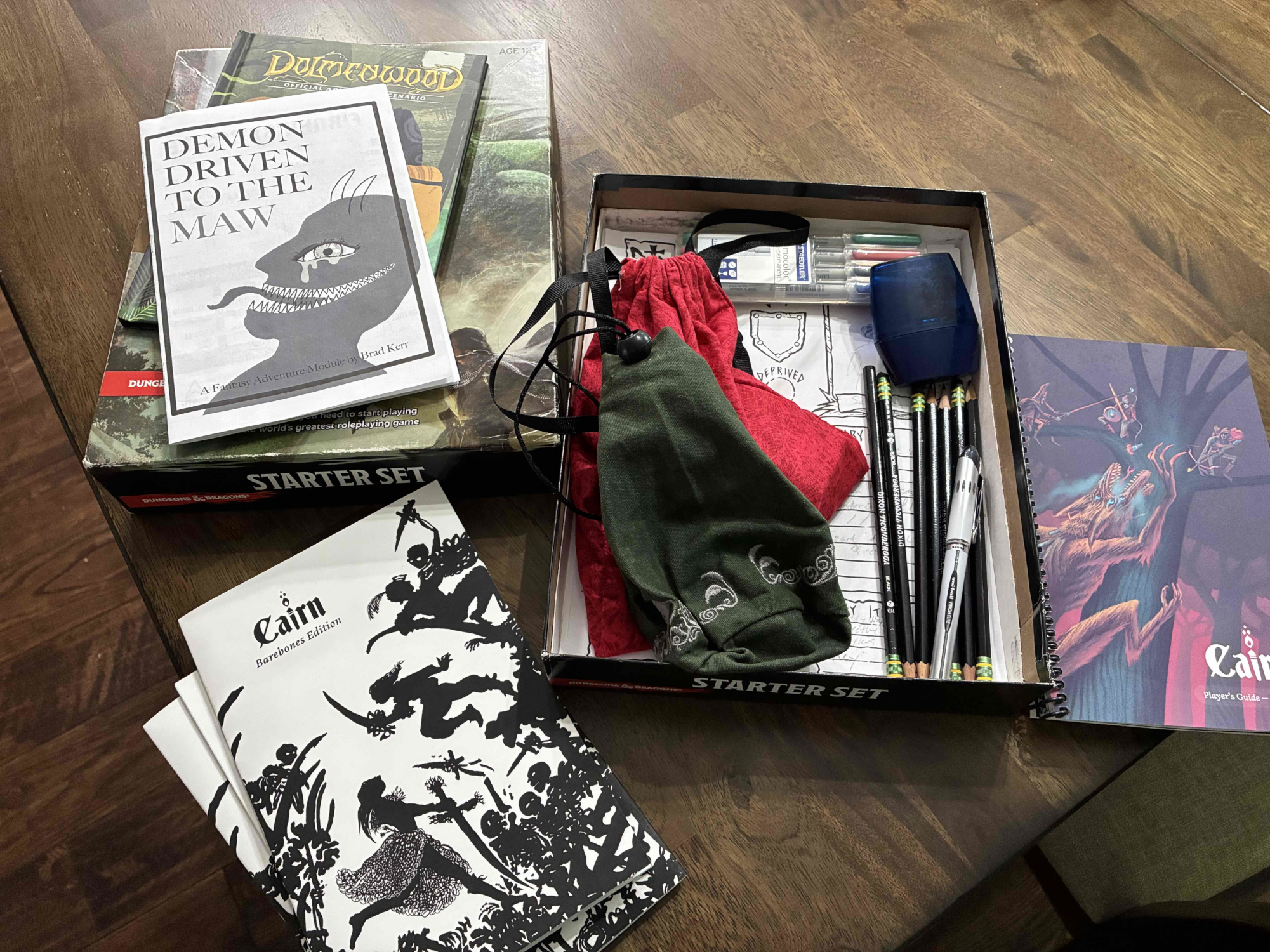 Picture of my TTRPG box with the Cairn books, dice, pencils, character sheets, and modules
